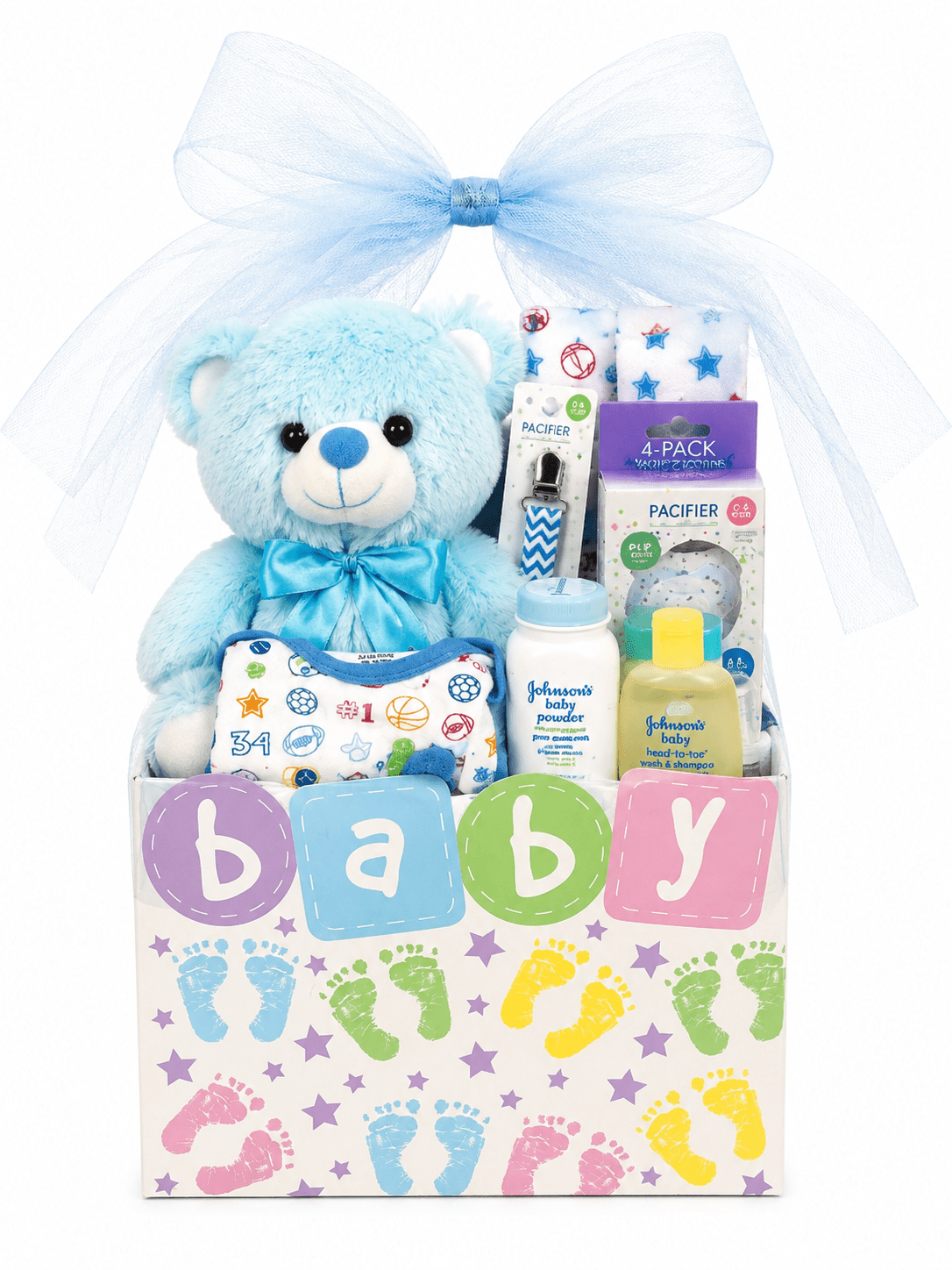 A baby gift basket set with a light blue plush teddy bear, a large white tulle bow, baby toiletries including Johnson's Baby items, pacifiers, and a small yellow bottle, arranged in a white box decorated with colorful letters spelling baby and pastel footprints.