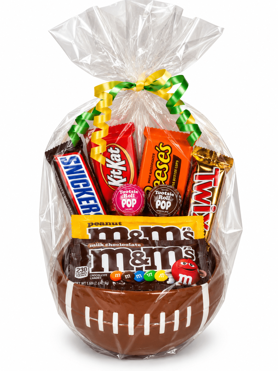 A chocolate and candy gift basket shaped like a football, wrapped in clear cellophane with a green and yellow ribbon. Visible candies include Snickers, KitKat, Reese's, Twix, M&M's, and Pop-Tarts.
